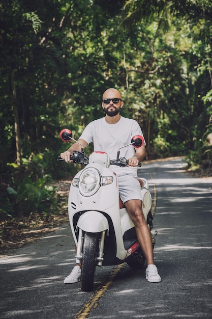 Stylish young man and his motorbike on the road in the jungle