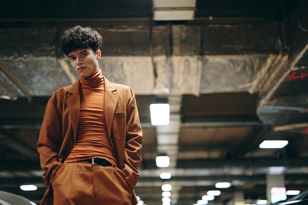 Stylish young man in modern brown outfit standing in an underground parking lot