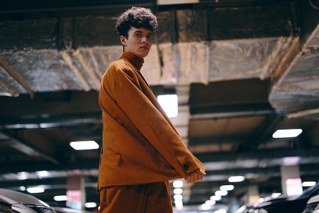 Stylish young man in an oversized orange outfit standing in a modern parking garage