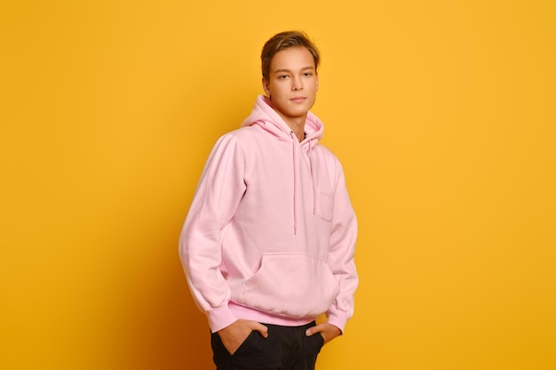 Stylish young man in pink sweatshot with hood posing over yellow studio background