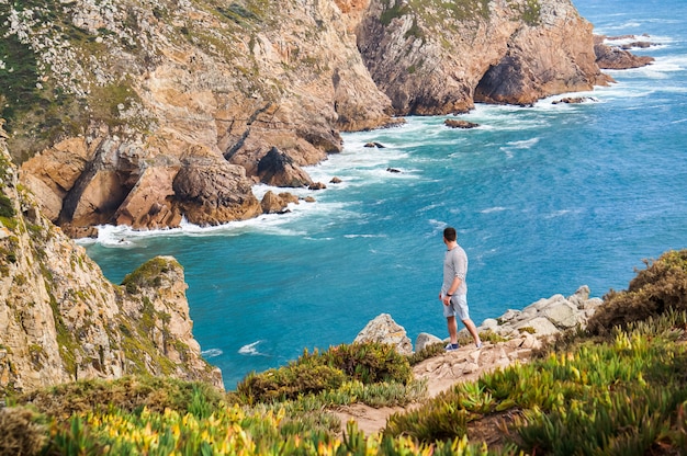 Stylish, young man standing at the very edge of the rock