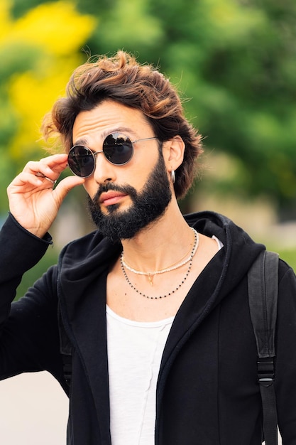 Stylish young man with beard putting on sunglasses