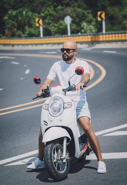 Stylish young man with his motorbike on the road