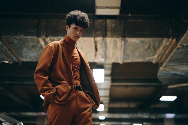 Stylish young person in a brown outfit posing in a dimly lit parking garage