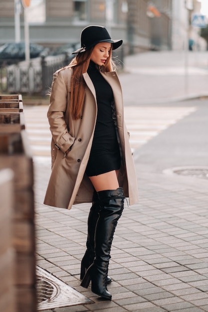 Stylish young woman in a beige coat in a black hat on a city street. Women's street fashion. Autumn clothing.Urban style.