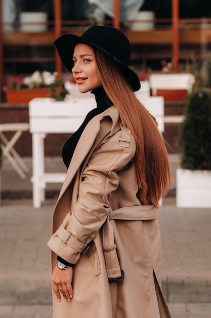 Stylish young woman in a beige coat in a black hat on a city street. Women's street fashion. Autumn clothing.Urban style.