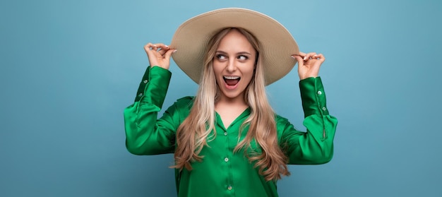 Stylish young woman exclaims in a summer hat with a brim on a blue studio background