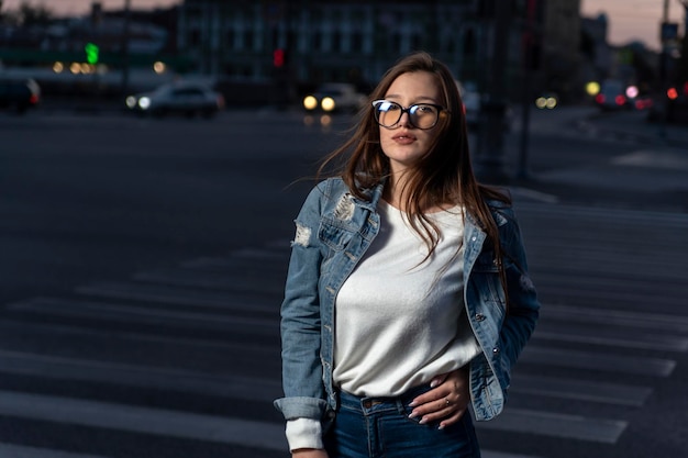 Stylish young woman in glasses on city street summer time Portrait of brunette girl in youth clothes on evening city