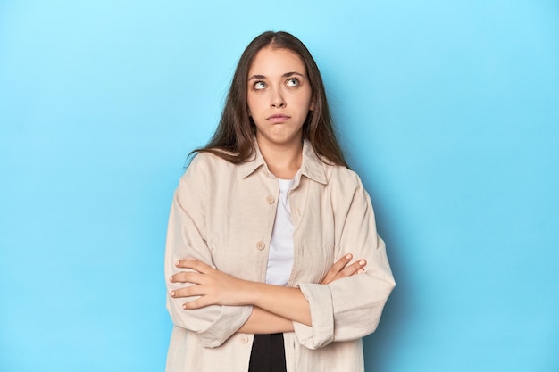 Stylish young woman in an overshirt on a blue background tired of a repetitive task