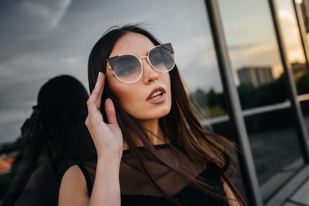 Stylish young woman posing in front of a business center in black. Fashion and style