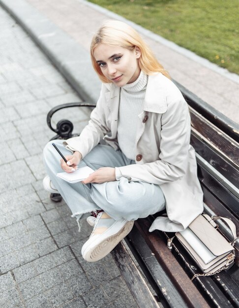 Stylish young woman tsudent sits on a bench and writes in notebook