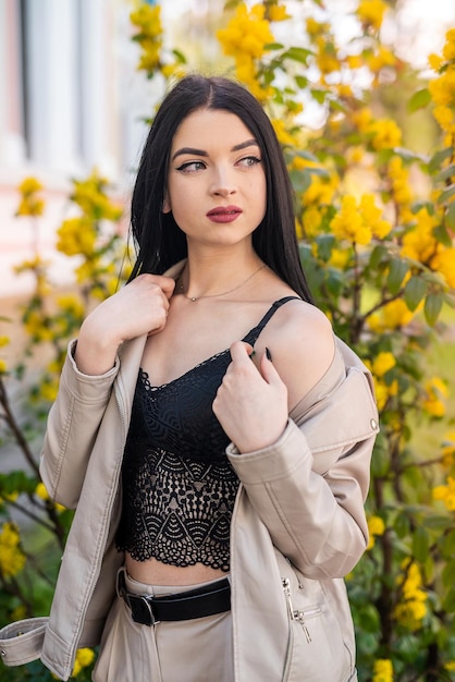 Stylish young woman in a white leather jacket posing near a cherry blossom in the spring garden