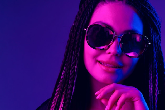 Stylish young woman with braids wearing sunglasses against purple background