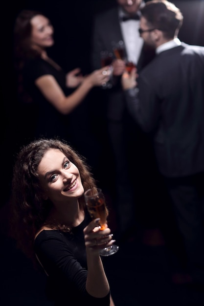 Stylish young woman with glass of champagne on the background of friends