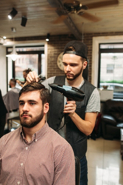 Stylist making modern hairdo for young man