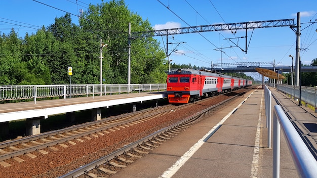 Suburban train arrives at station in summer on sunny day. Railway platform with train en route.