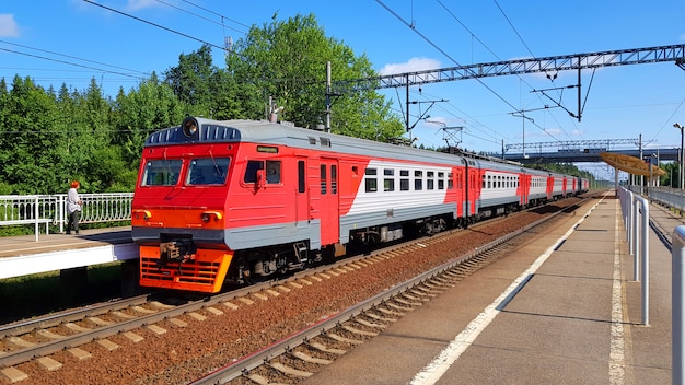 Suburban train arrives at station in summer on sunny day. Railway platform with train en route.