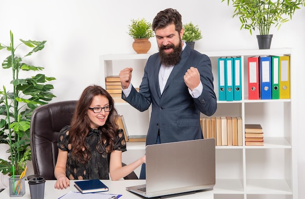 Success attends hard work. Colleagues celebrate success. Happy man and woman in office. Boss make winning gesture. Secretary work on laptop. Together we achieve more.