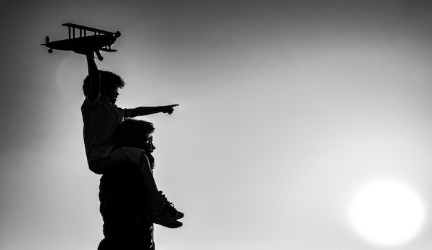 Success and child leader concept Sunset silhouette of Father and son together Boy child is sitting on daddy shoulder piggyback while the flight