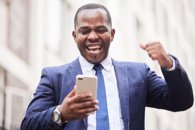 Success phone or happy businessman in a city in celebration of good news job promotion or sales goals Winner wow or excited black man celebrates winning a bonus or successful financial investment