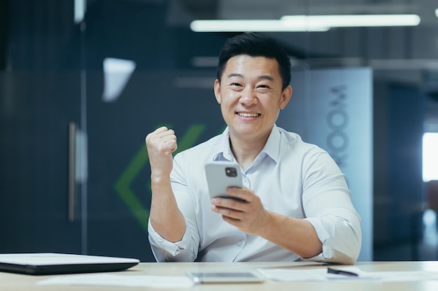 Success win young asian business man holds phone in hand rejoices win good news reads message