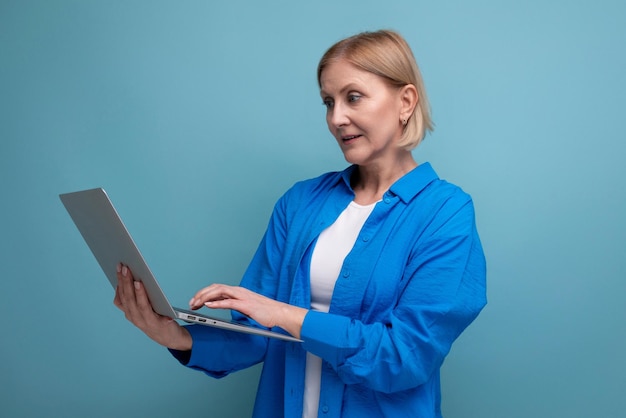 Successful adult business woman working remotely using laptop on blue background with copy space