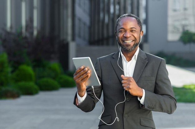 Successful african american boss outside office building with tablet computer and headphones talking