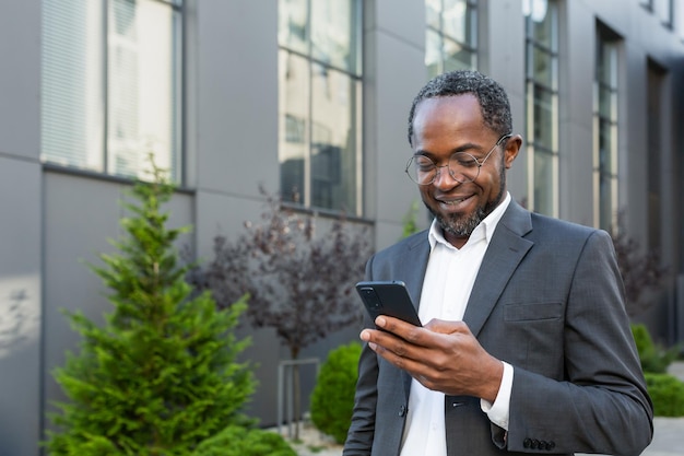 Successful african american businessman outside modern office building in business suit using