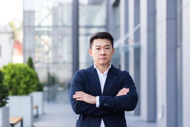 Successful asian boss near office looking at camera with crossed arms of serious businessman