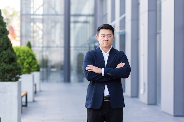 Successful asian boss near office looking at camera with crossed arms of serious businessman