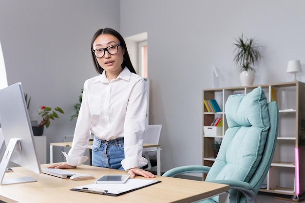 Successful Asian business woman at workplace in office looking at camera portrait of strong leader