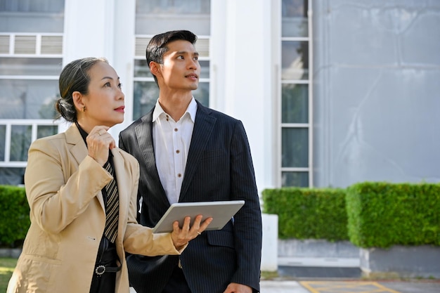 Successful asian businessman and aged businesswoman standing outside of the building