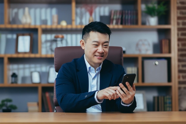 Successful Asian businessman working in the office sitting at the table typing on the phone happy and smiling