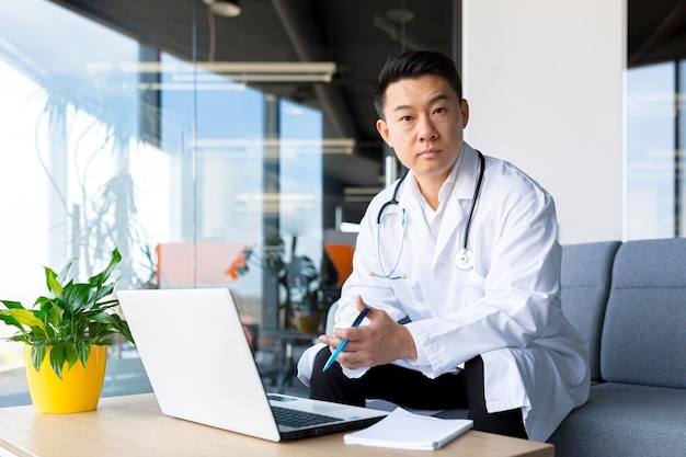 Successful Asian doctor working on a laptop in a modern clinic