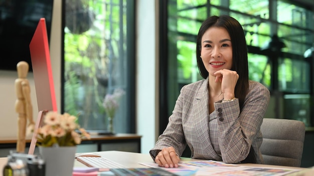 Successful asian female entrepreneur sitting at creative office and smiling to camera