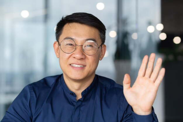 A successful asian man inside the office is looking at the web camera talking on a video call with