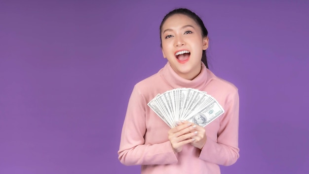 Successful beautiful Asian business young woman holding money US dollar bills in hand isolated on purple background with copy space business concept