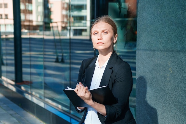 Successful beautiful business woman standing against backdrop buildings writes