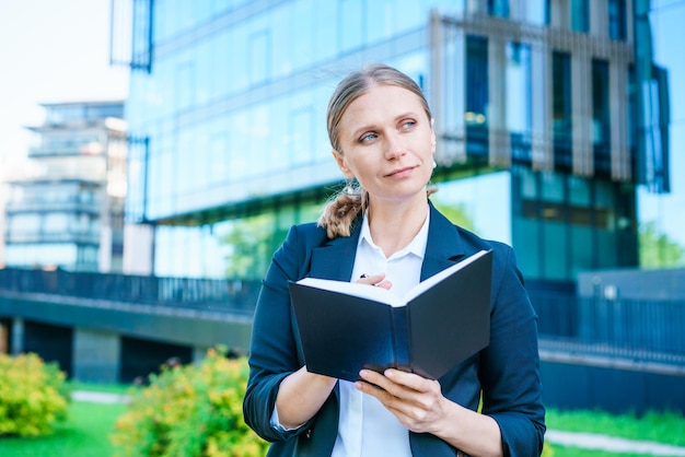 Successful beautiful business woman standing against backdrop buildings writes