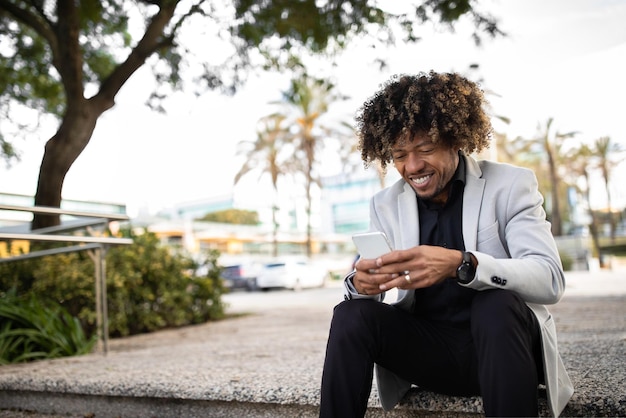 Successful black middle aged male entrepreneur using cellphone texting or browsing internet sitting