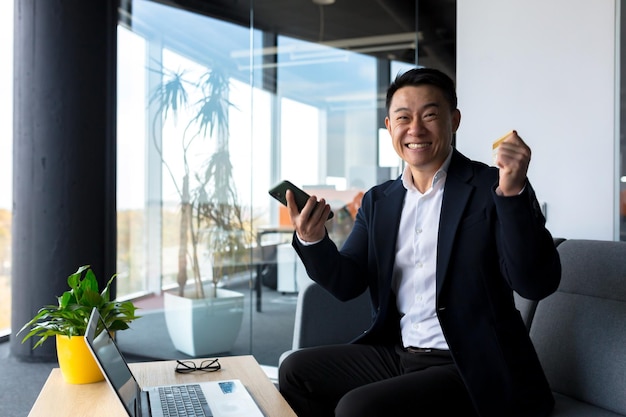 Successful business man rejoices in victory and successful sales contract smiles looks at camera in modern office boss SEO celebrates winning