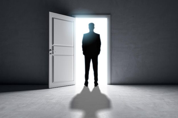 Successful business man standing in front of bright success door in concrete interior with shadow on floor Future and dream concept