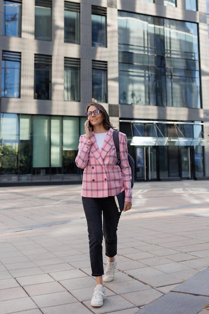 Successful business woman in a pink jacket and glasses goes to the office to work and talks on the phone