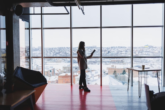 Successful business woman standing looking out the window enjoying the city view confident wealthy leader woman thinking about business success and vision for the future planning new goals