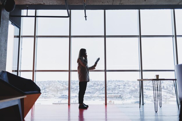 Successful business woman standing looking out the window enjoying the city view confident wealthy leader woman thinking about business success and vision for the future planning new goals