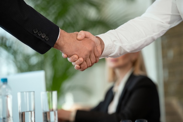 Successful businessman in formalwear greeting his foreign partner by handshake against secretary after negotiating and making deal