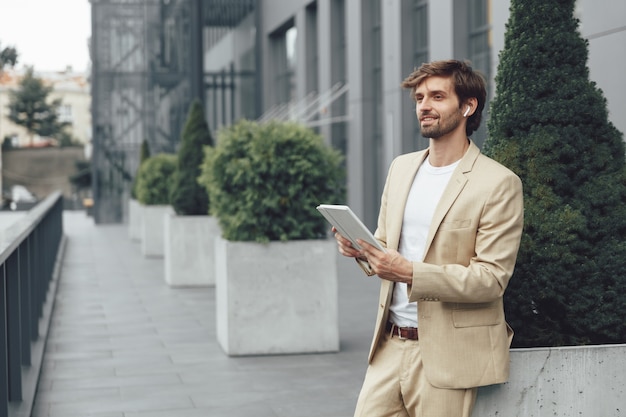 Successful businessman standing on street and using digital tablet for online working meeting