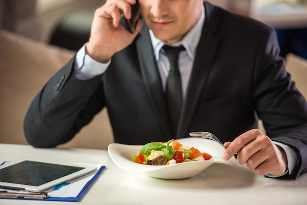 Successful businessman in suit sitting in cafe and eating salad