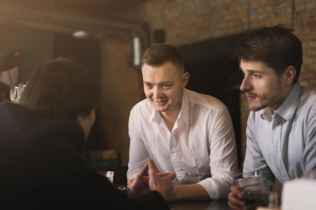 Successful businessmen drinking beer and talking with barman at the bar. Confident men having fun and rest, copy space