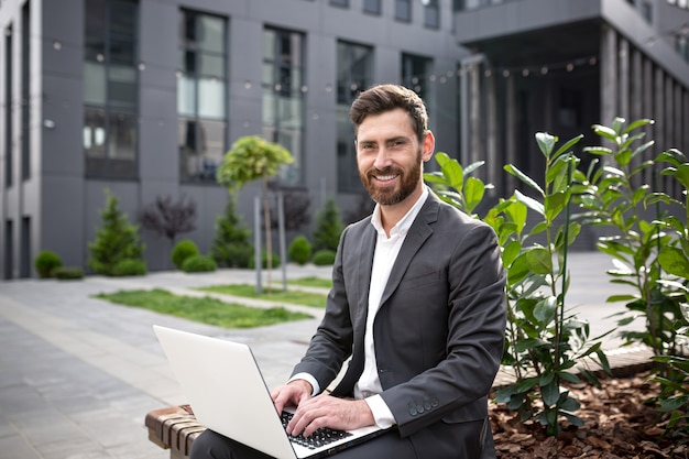 Successful businesswoman, man looking at camera and smiling happy working on laptop in park on bench at lunchtime